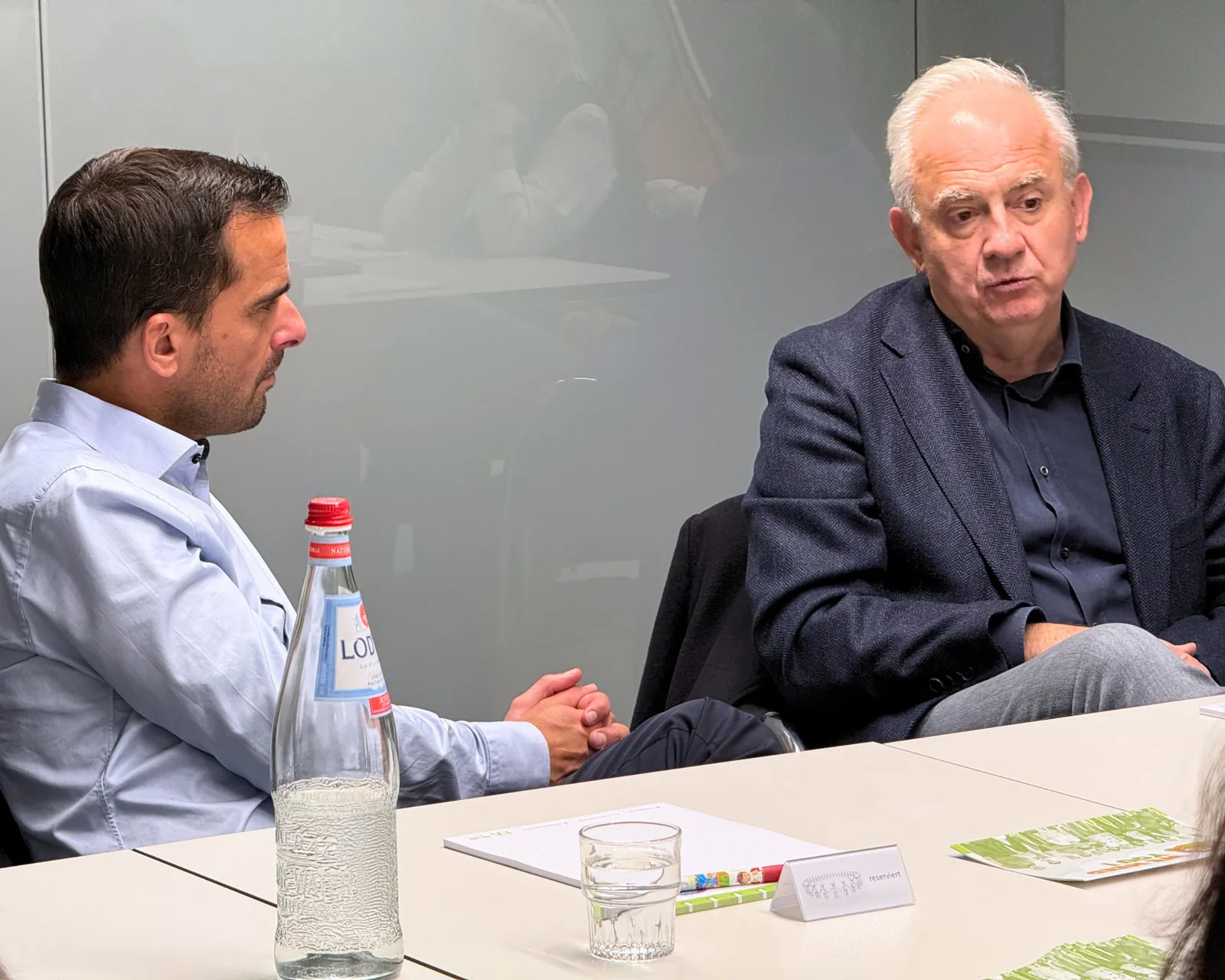 Échange entre deux invités à la table de réunion lors de la visite du Ministre Max Hahn au service Super Senior du MEC asbl